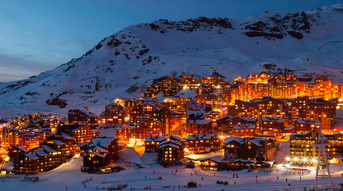 Ski resort and chalets at night lit up with yellowing lights at the base of a snowy mountain